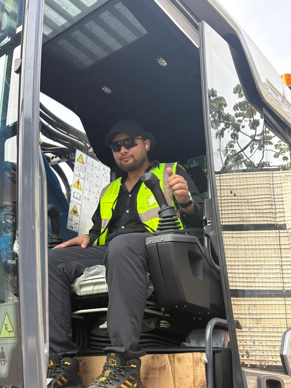 Yard operator in a safety vest and sunglasses seated in the MHL 350 cab with a hand on the joystick, giving a thumbs up